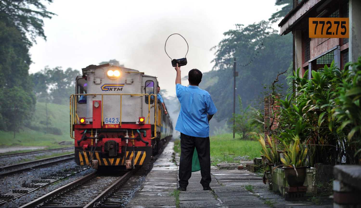 シンガポールの物語 - 真鍮のトークンを渡す用意をするKTM鉄道の駅長