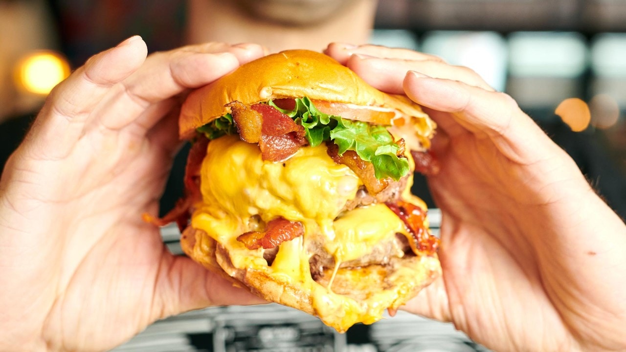 Man holding onto a burger from Black Tap's 2024 Father's Day dinner menu